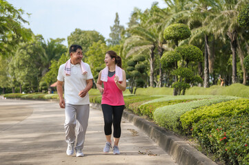 Asian Elderly Father and Daughter are jogging and relaxing in a green park, Breathing in the fresh air and enjoying the beautiful scenery. Health care and family bonding.