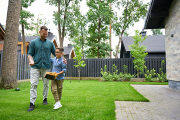 Father and son walk along the green grass near house
