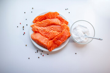 Fresh raw salmon fish fillet on a white plate, a small bowl of salt and black peppercorns on white background. Healthy food.