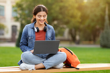Indian young woman student sitting on bench working on laptop