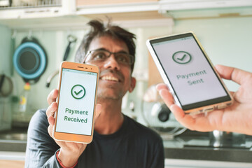 A smiling South Asian man showing a message of successful payment from his friend. Instant digital money transfer or real-time payment concept. - obrazy, fototapety, plakaty