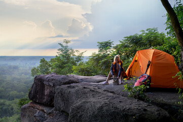 Female Travelers Pitch Vibrant Orange Tent on Cliff with a Natural View. Setting Camping Stove on Cliff, Embracing Pristine Natural Views or Surrounded by Cliffside Beauty in Trekking Trip.