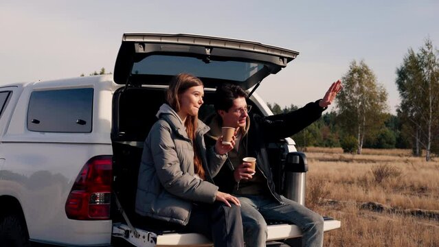A guy and a girl are sitting together in the open trunk of a crossover talking and squinting from the sun in nature in forest steppe