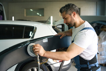 Experienced car detailer buffing car bumper in workshop