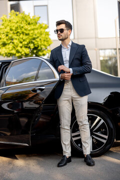 Portrait of a handsome businessman standing near luxury car outdoors. An elegant man gets out of a premium car