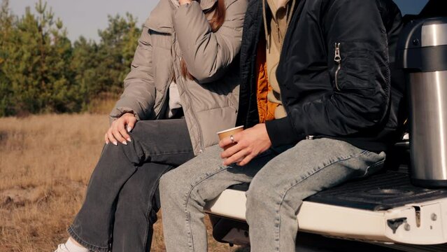 A guy and a girl are sitting together in the open trunk of a crossover talking and squinting from the sun in nature in forest steppe