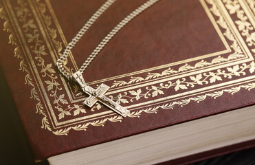 Silver necklace with crucifix cross on christian holy bible book on black wooden table. Asking...