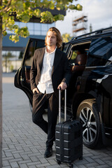 Portrait of a young businessman stand with a suitcase near car outdoors. Concept of business trip...