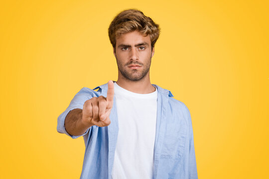 Focused European man touches invisible tech screen on yellow. background