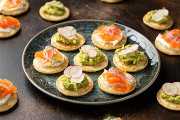 Mini blini pancakes with soft cheese, cold smoked salmon and guacamole