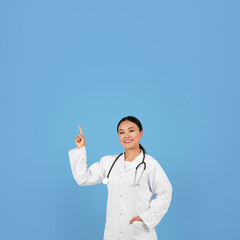 Smiling Asian Female Doctor Pointing Finger Up At Copy Space Above Head