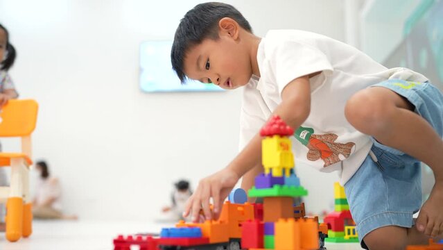 Adorable kindergarten 5 year boy playing color plastic block toy construction site building with transport industry