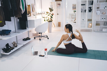 Slim woman sitting on mat and doing online yoga - obrazy, fototapety, plakaty