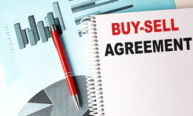 BUY-SELL AGREEMENT text on a notebook with pen on a chart background