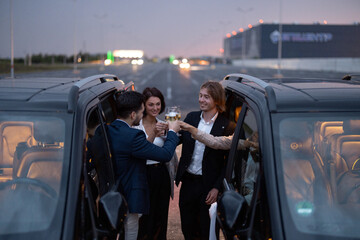 Group of business partners have fun together, drinking alcohol while celebrating between cars on...