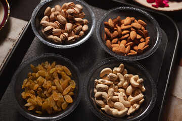 There are dry fruits arranged in a black bowl which is placed on a black tray.