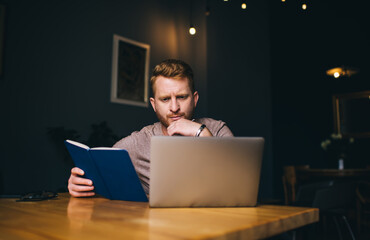 Caucasian bearded student making online research via modern laptop technology using coworking...