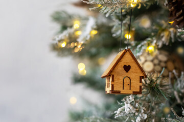Christmas tree toy in the form of a house on a branch. Concept house insurance, house gift. Christmas mood background. Family budget. Mortgage buying real estate.