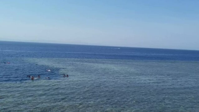 Some people are snorkelling in the Blue Hole, Dahab, South Sinai, Egypt. There is a launch moving near them. The Blue Hole is famous for snorkelling and diving. It's called Diver's Cemetery.