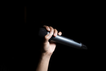 Male hand holding microphone  isolated on black background - obrazy, fototapety, plakaty
