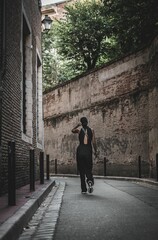 Brunette woman wearing black overalls and white sneakers walking in an alleyway with brick walls