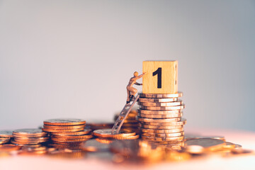 Miniature people, man on a ladder try to grab number one wooden box on stack coins using for business and financial concept