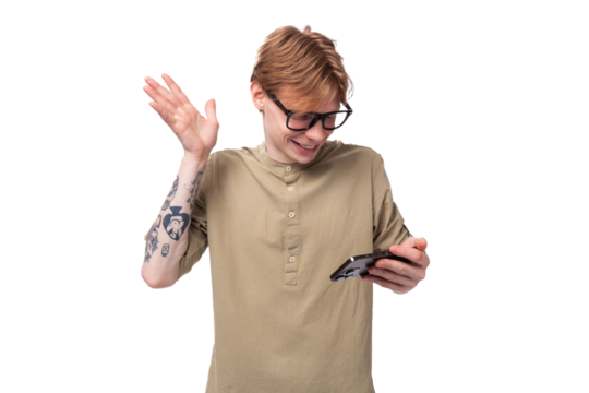 young charming caucasian guy with red hair in khaki shirt smiling while looking at the phone