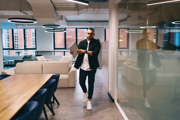 Confident businessman walking in modern office with laptop