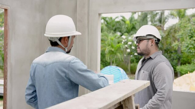 Two Asian men, construction engineers, standing talking in house that is only 50% completed, let's talk about reasons why this happened correct solutions, make customers satisfied with building house.