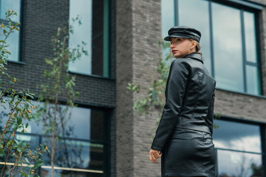 Trendy beauty young stylish woman in leather black jacket, skirt and hat posing on the street on the urban background.