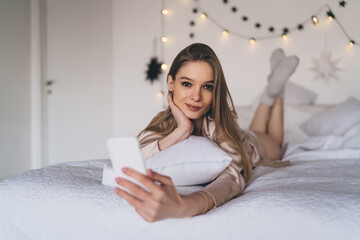 Smiling woman with dark hair using smartphone on bed