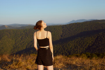 a beautiful, slender woman is resting in the mountains, standing in summer clothes