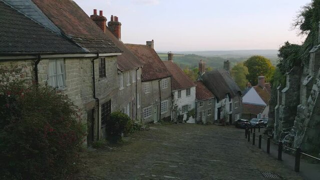 Gold Hill Shaftesbury England.  Location of iconic Hovis Bread commercial by Ridley Scott. Evening sunshine on a summers day, steep cobbled street in England.  Drone tracks up the hill.  No.1 of 6.