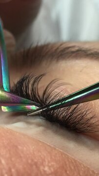 Unrecognizable woman eye close-up on eyelash extension procedure. Cropped video. The master checks his work for gluing. Vertical video. 