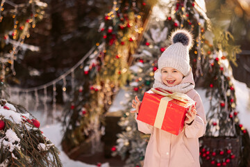 Little girl with a Christmas gift outdoors in winter on Christmas Eve. New Year background for holiday sale or promotion.