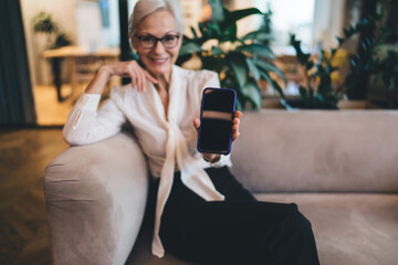 Smiling aged businesswoman showing positive result on smartphone