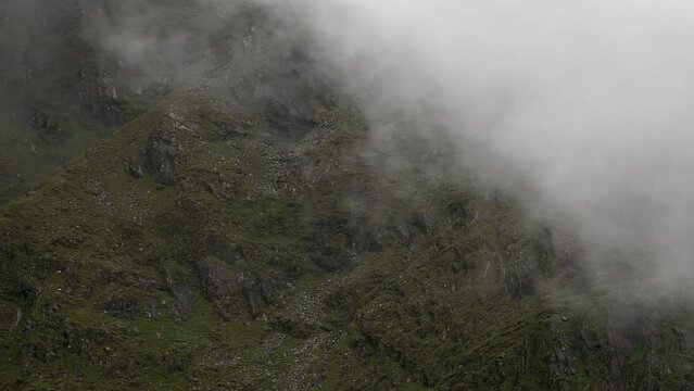 The mountainous terrain, enveloped in mist and punctuated by rugged rocks, sets a compelling and moody scene. pano