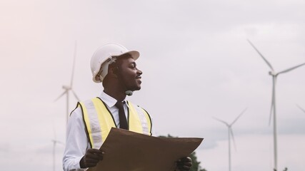 Successful african engineer man stands with smile front the wind turbines generating electricity...