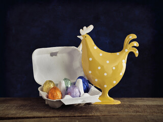 Yellow metal chicken with colourful Easter eggs in egg box.