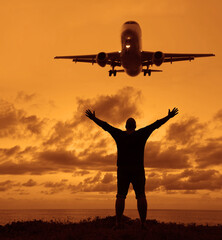One man watching the landing airplane. Silhouette of a man with raised-up arms at the sunset. male raised hand in air with success goal on sunset background. guy standing on coast. freedom. hands up