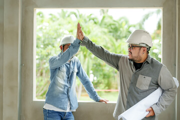 Fototapeta na wymiar Two men, employee, engineer and architect, designer Manager, foreman, Asian male Tack your hands to prepare to start work on the house structure. Wear white safety helmet prevent things from falling.