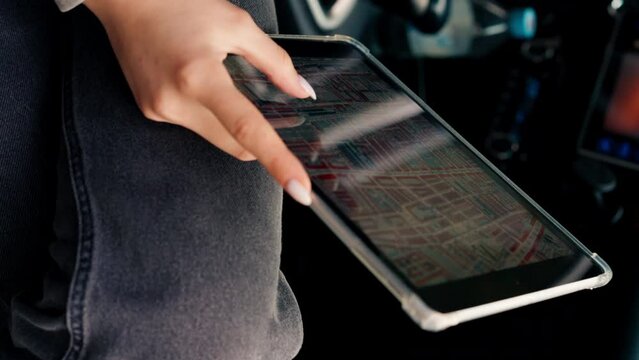 Close-up shot of a girl sitting in a car plotting a route through the forest using map on a tablet