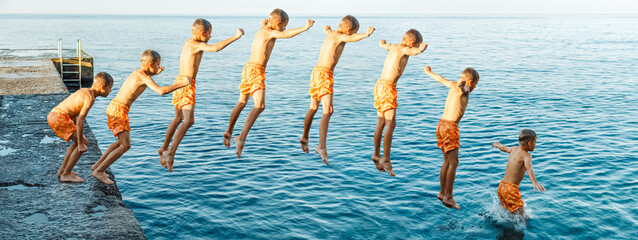 Sequence of jump. Moments of schoolboy jumping from stone pier into sea at sunrise doing tricks in...
