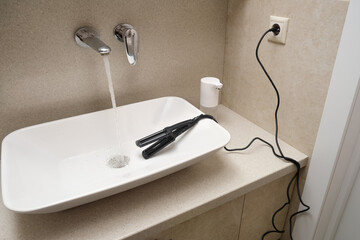 An electrical appliance lies dangerously in a sink with running water. Electrical shock can occur...