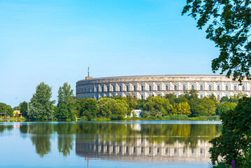 The famous "Kongresshalle" (meaning: Congress Theater), in Nuremberg, Bavaria, Germany, typical of the nazi period, reflecting in a symmetrical view on the blue waters. Sky on the background.