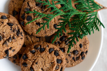 Chocolate cookies on a plate with spruce branches on the table. Dark chocolate cookies on a plate,...