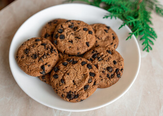 Chocolate cookies on a plate with spruce branches on the table. Dark chocolate cookies on a plate, Christmas cookies chocolate cinnamon sweet dessert holiday treat new year and christmas food
