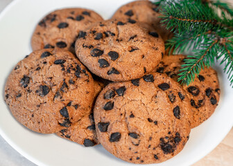 Chocolate cookies on a plate with spruce branches on the table. Dark chocolate cookies on a plate,...