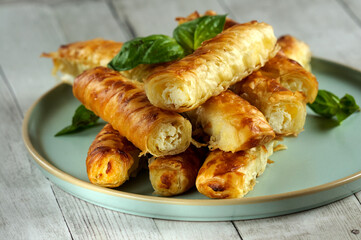 Pastries in the form of puff pastry tubes filled with cheese or cottage cheese with basil leaves. Natural light, selective focus