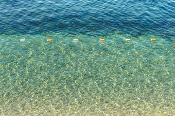 Safety buoys line floats on transparent water surface at sea resort. Marking for swimmers on clear ocean on sunny day. Calm seaside scene